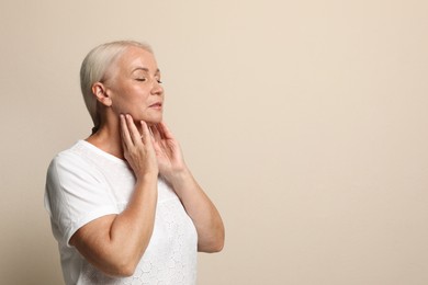 Photo of Mature woman doing thyroid self examination on beige background, space for text
