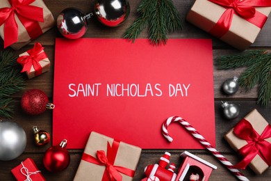 Photo of Card with phrase Saint Nicholas Day, gift boxes and festive decor on wooden table, flat lay