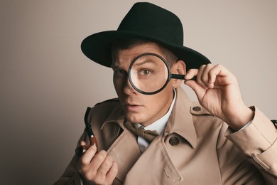 Male detective with smoking pipe looking through magnifying glass on beige background