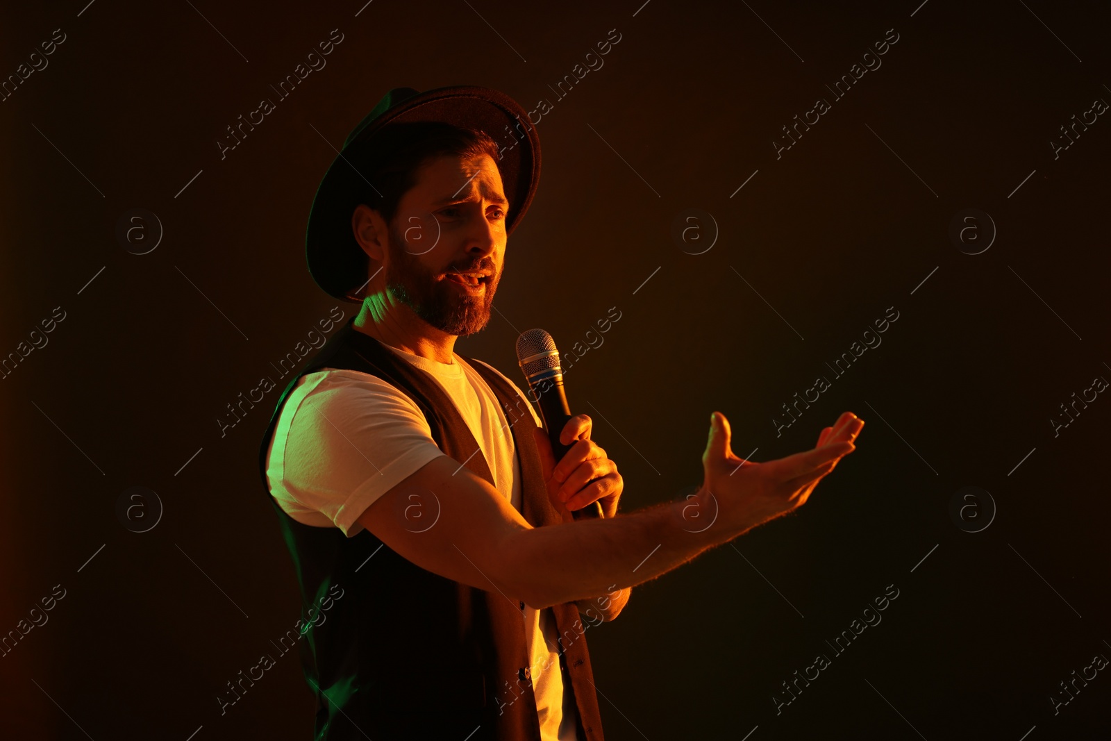 Photo of Handsome man with microphone singing in neon lights on dark background