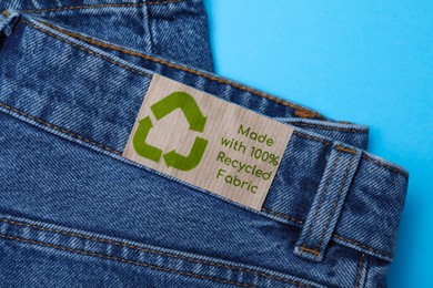 Photo of Jeans with recycling label on light blue background, closeup