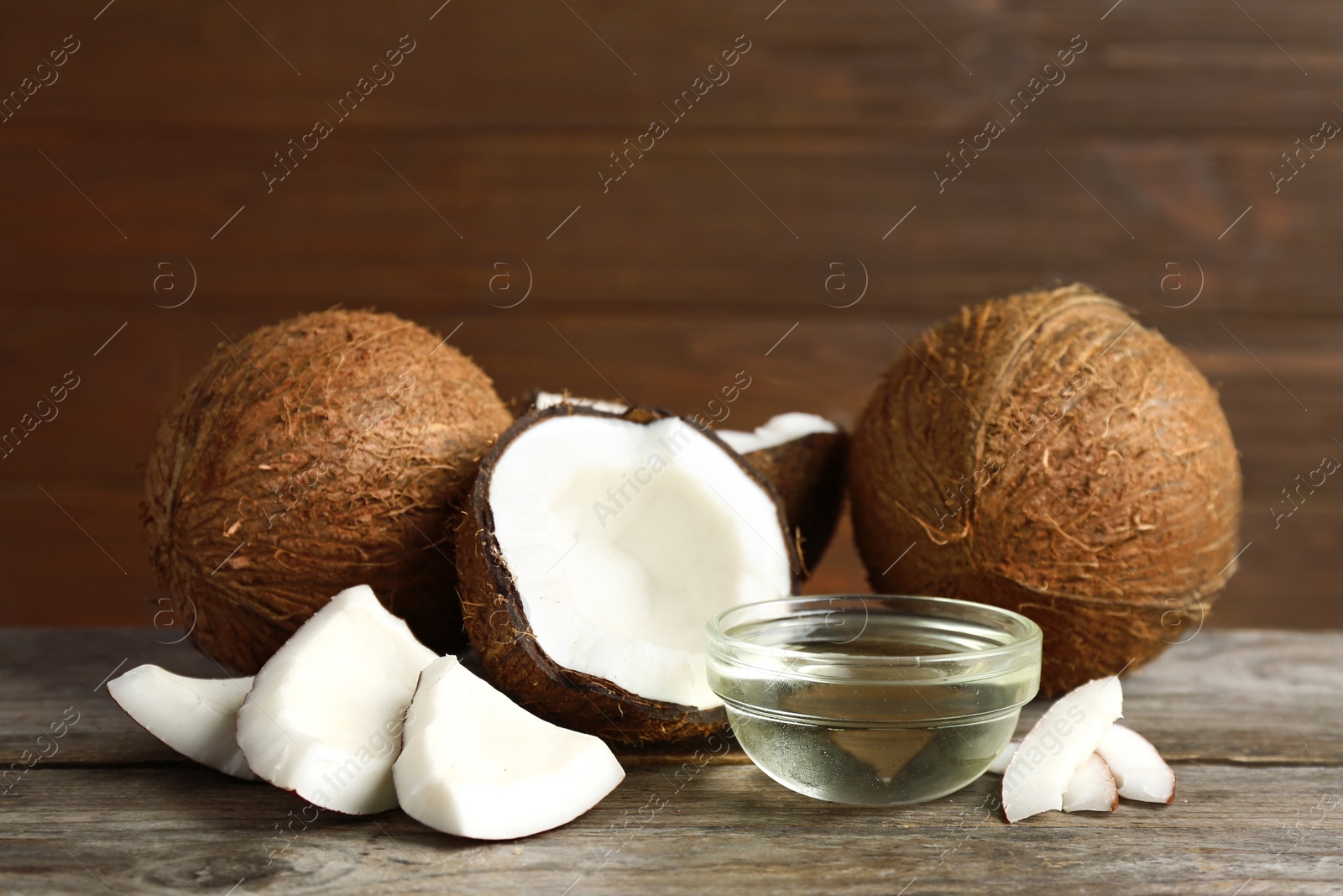 Photo of Bowl of natural organic oil and coconuts on brown wooden table