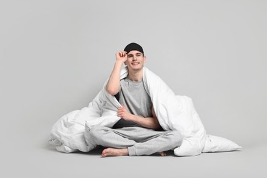 Photo of Happy man in pyjama and sleep mask wrapped in blanket on grey background