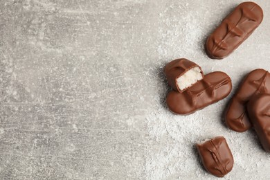 Delicious milk chocolate candy bars with coconut filling on grey table, flat lay. Space for text