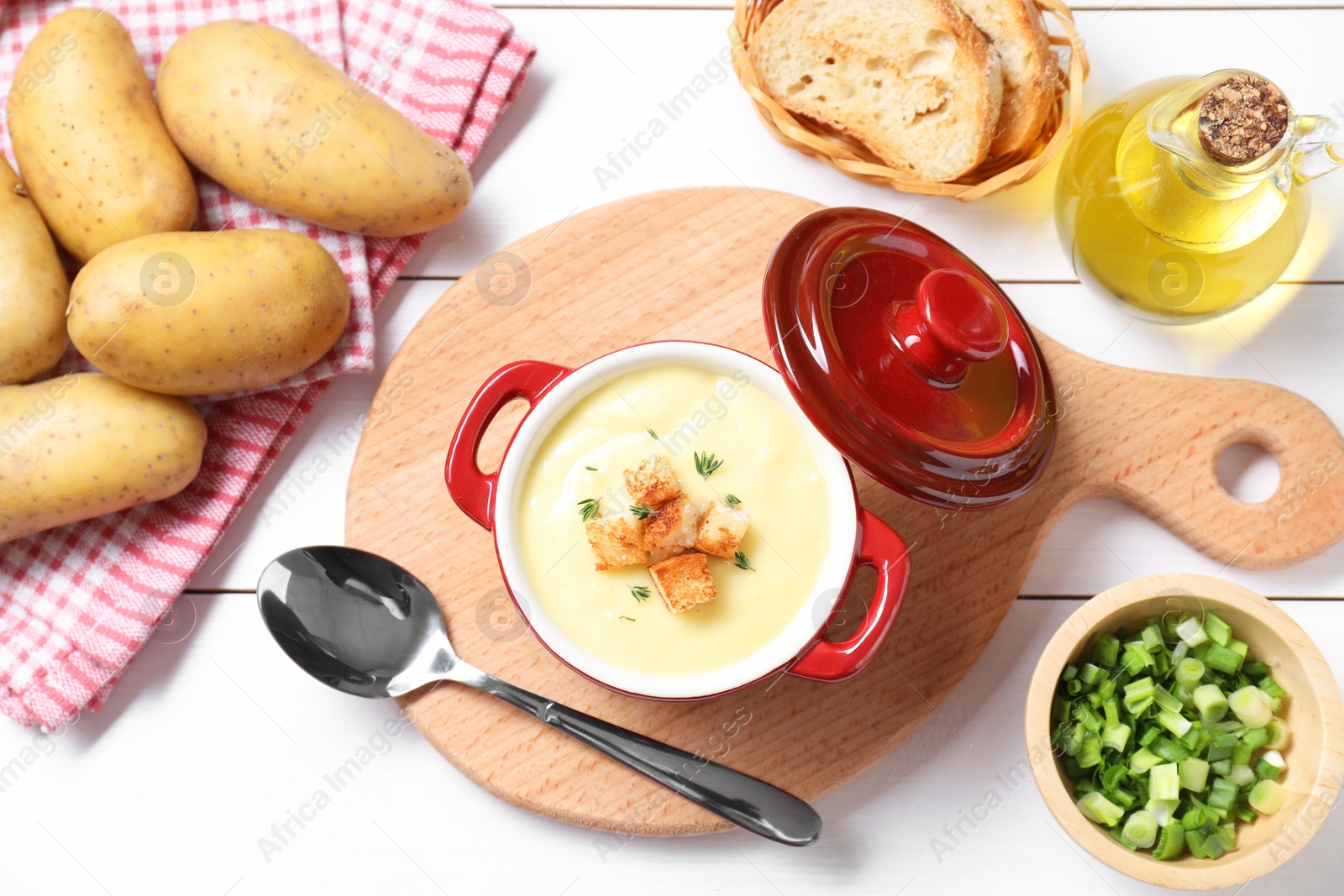 Photo of Tasty potato soup with croutons and rosemary in ceramic pot served on white wooden table, flat lay