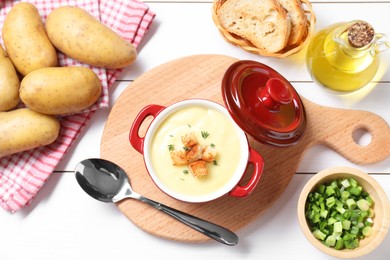 Tasty potato soup with croutons and rosemary in ceramic pot served on white wooden table, flat lay