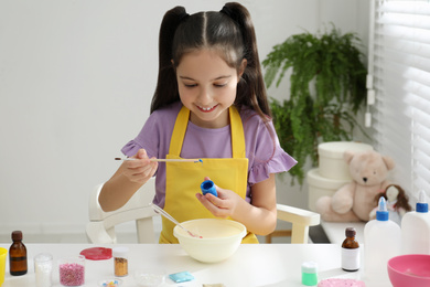 Photo of Cute little girl making homemade slime toy at table in room