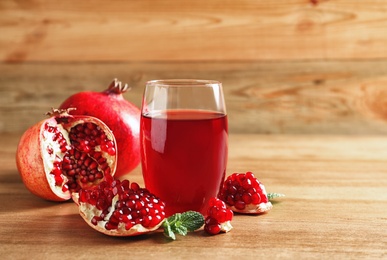 Photo of Glass of pomegranate juice and fresh fruits on wooden table, space for text