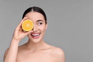 Photo of Beautiful young woman with piece of orange on grey background. Space for text
