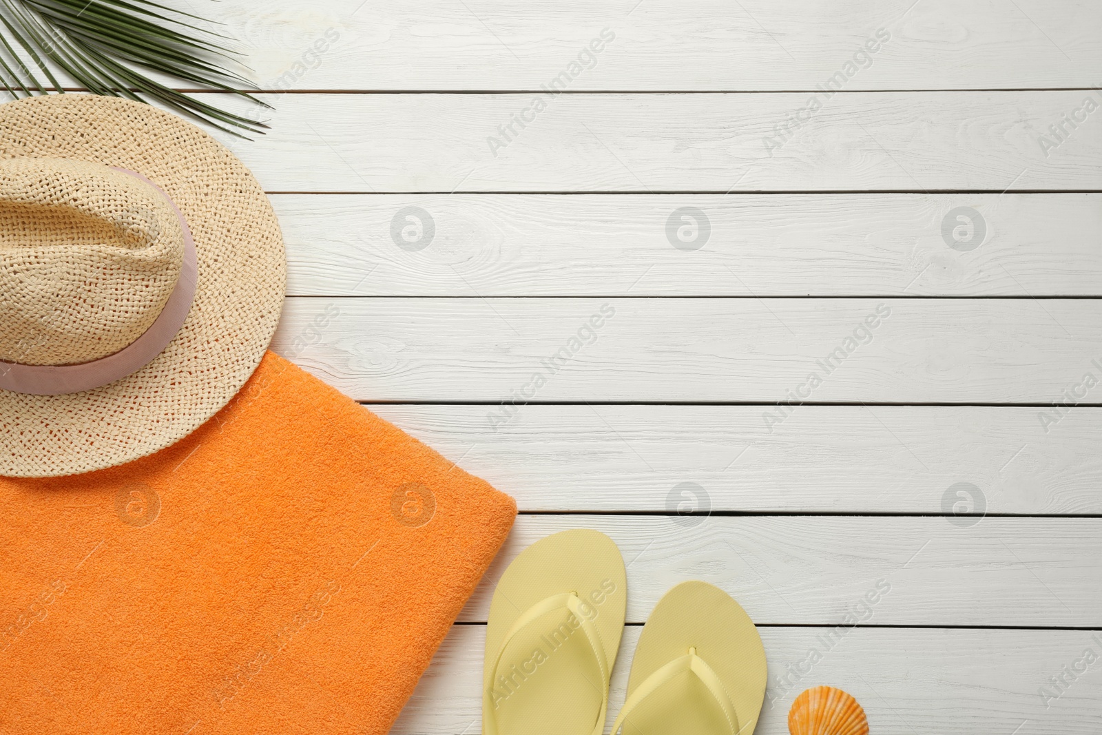 Photo of Beach towel, flip flops and hat on white wooden background, flat lay. Space for text