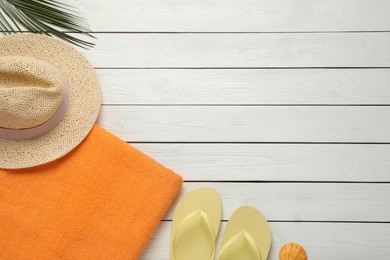 Photo of Beach towel, flip flops and hat on white wooden background, flat lay. Space for text