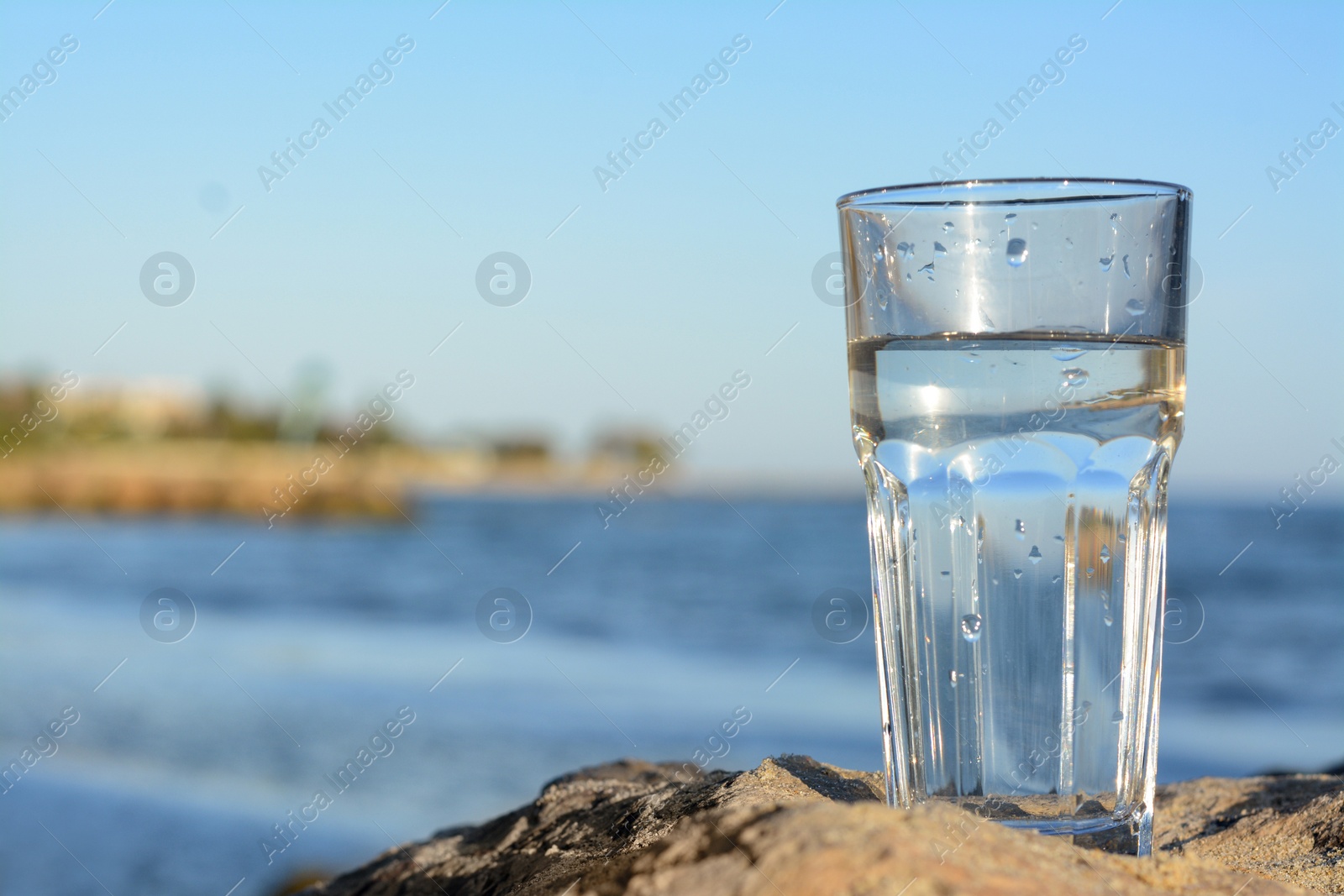 Photo of Glass of clean water on rock near sea. Space for text