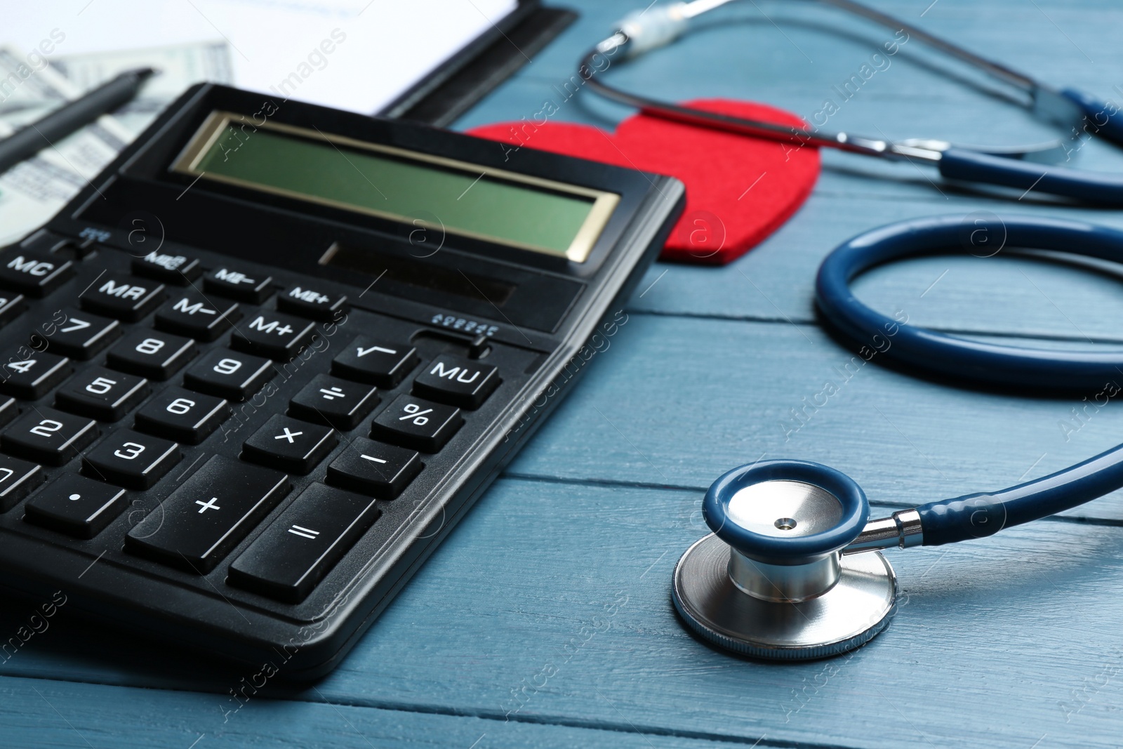 Photo of Calculator and stethoscope on blue wooden surface. Health insurance concept