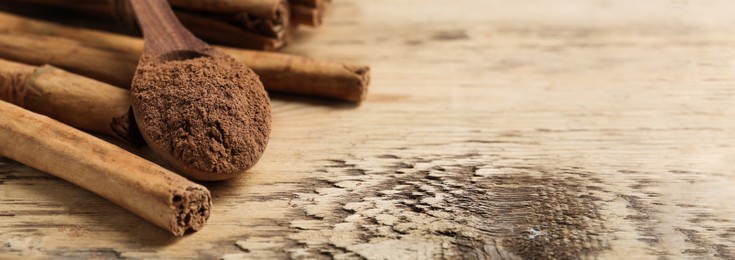 Image of Aromatic cinnamon powder and sticks on wooden table, closeup view with space for text. Banner design