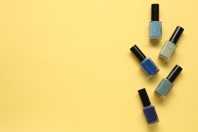 Bright nail polishes in bottles on yellow background, flat lay. Space for text