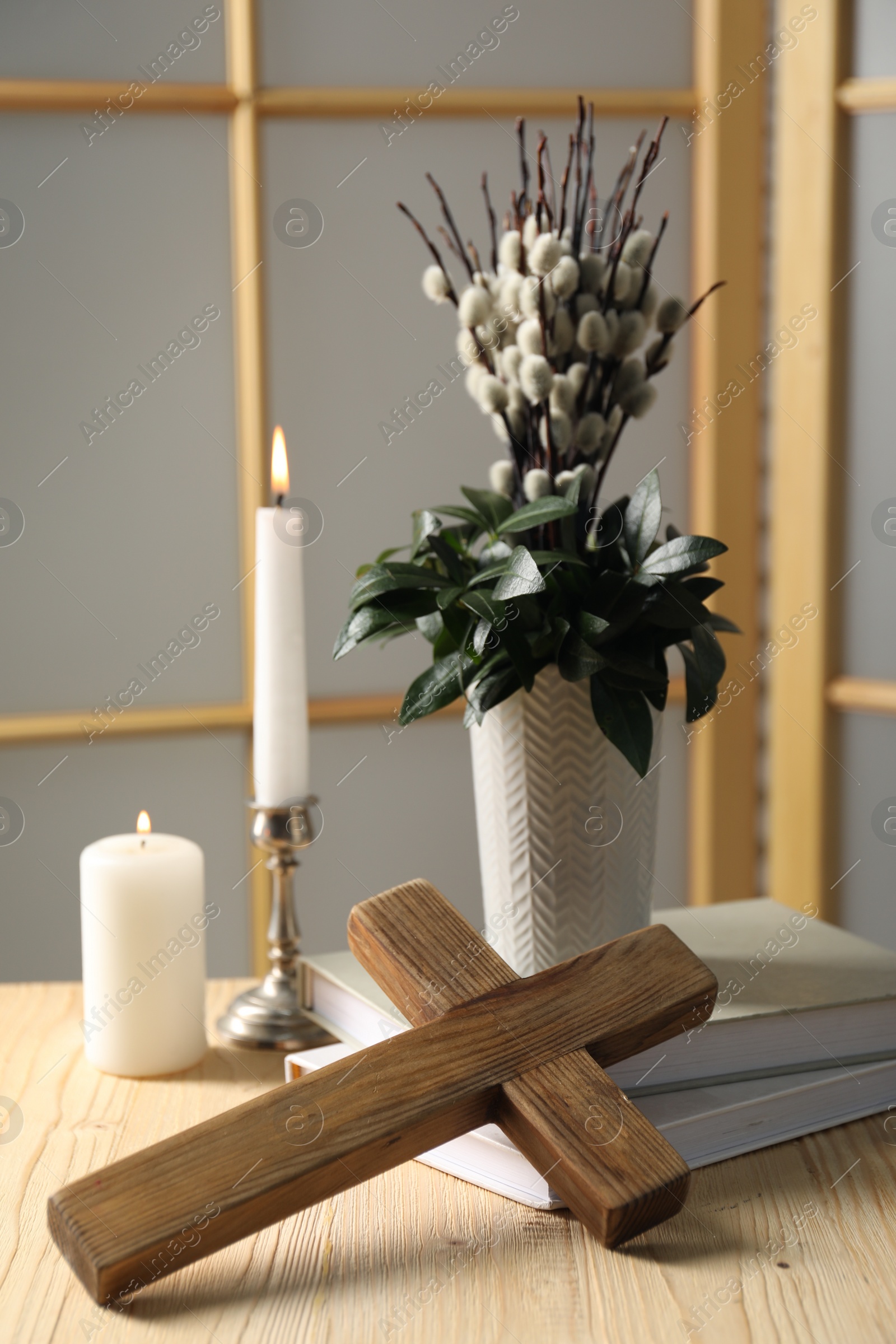 Photo of Cross, burning candles, books and bouquet with willow branches on wooden table