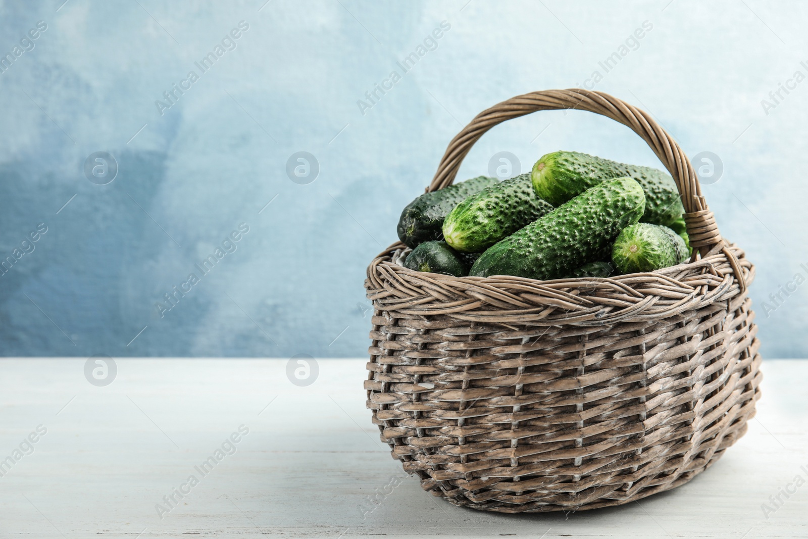 Photo of Wicker basket with ripe fresh cucumbers on table