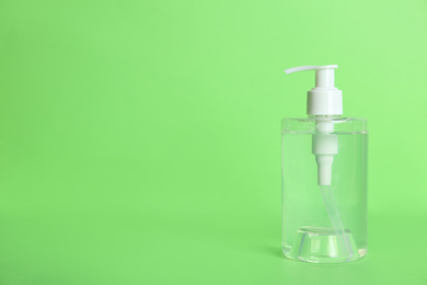 Photo of Dispenser bottle with antiseptic gel on green background. Space for text