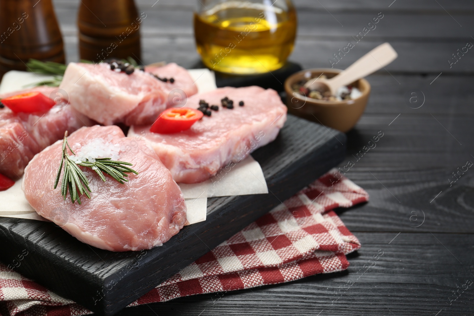 Photo of Pieces of raw pork meat with chili pepper and spices on black wooden table. Space for text