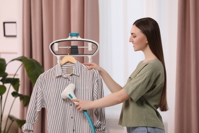 Photo of Woman steaming shirt on hanger at home