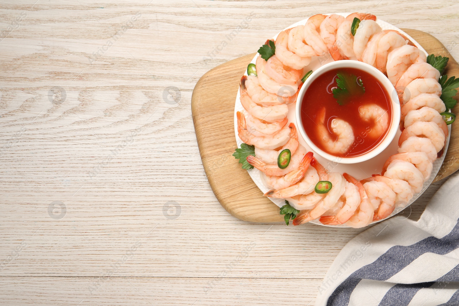 Photo of Tasty boiled shrimps with cocktail sauce, chili and parsley on light wooden table, top view. Space for text