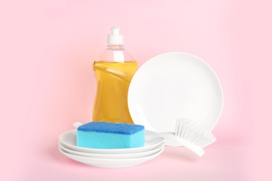 Photo of Detergent, plates and sponge on pink background. Clean dishes