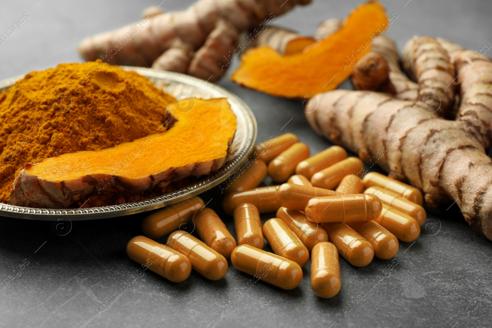 Photo of Aromatic turmeric powder, pills and raw roots on grey table, closeup