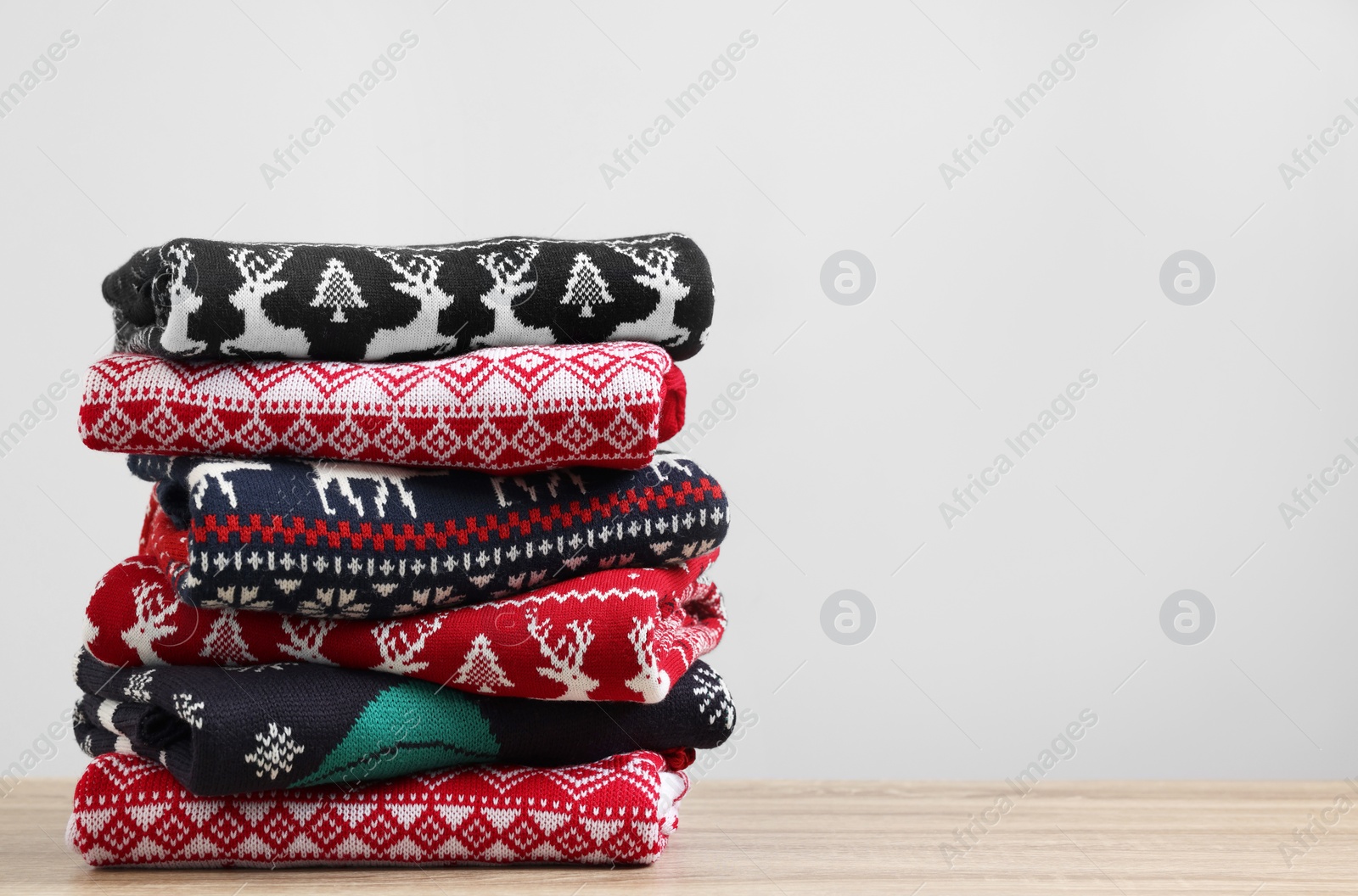 Photo of Stack of different Christmas sweaters on wooden table against light background. Space for text