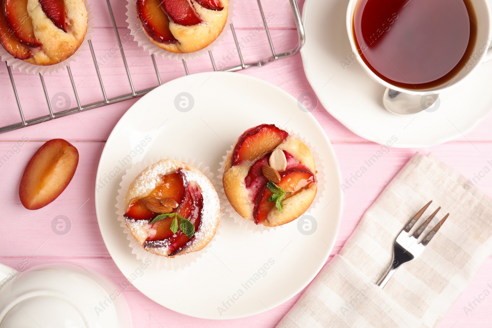 Photo of Delicious cupcakes with plums on pink wooden table, flat lay