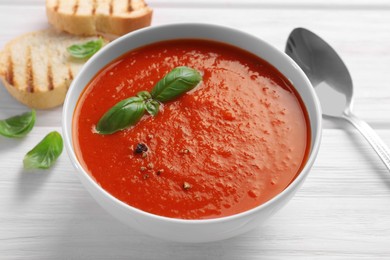 Delicious tomato cream soup in bowl on white wooden table, closeup