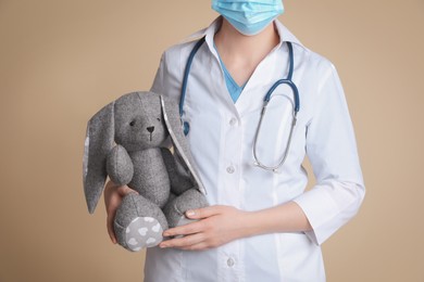 Photo of Pediatrician with toy bunny and stethoscope on beige background, closeup