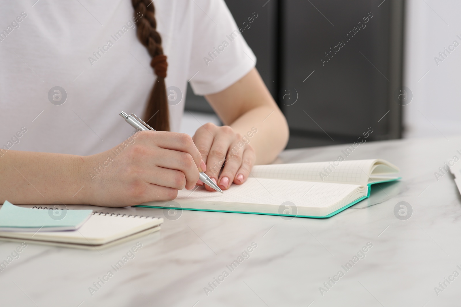 Photo of Woman writing in notebook at white marble table indoors, closeup