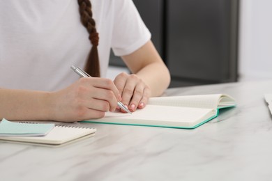 Woman writing in notebook at white marble table indoors, closeup