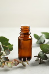 Photo of Bottle of eucalyptus essential oil and leaves on white table