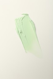 Photo of Stroke of green color correcting concealer on white background, top view
