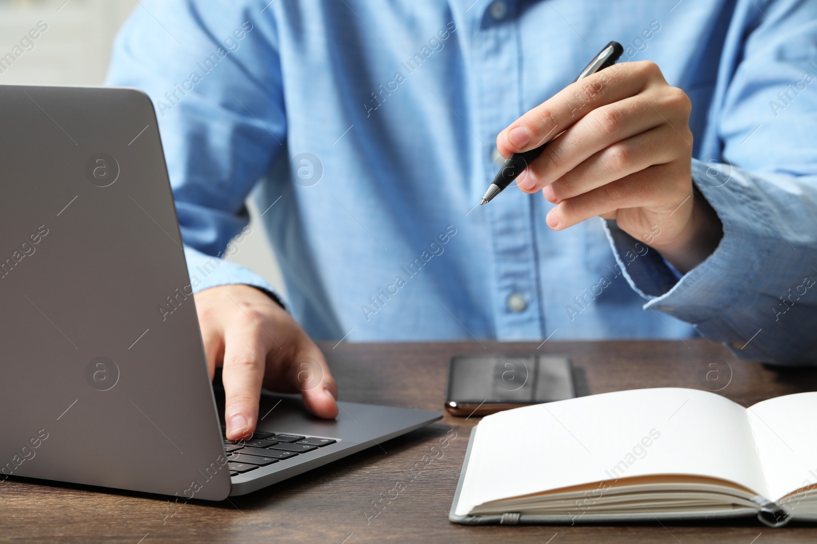 Photo of Man with pen and laptop at wooden table, closeup