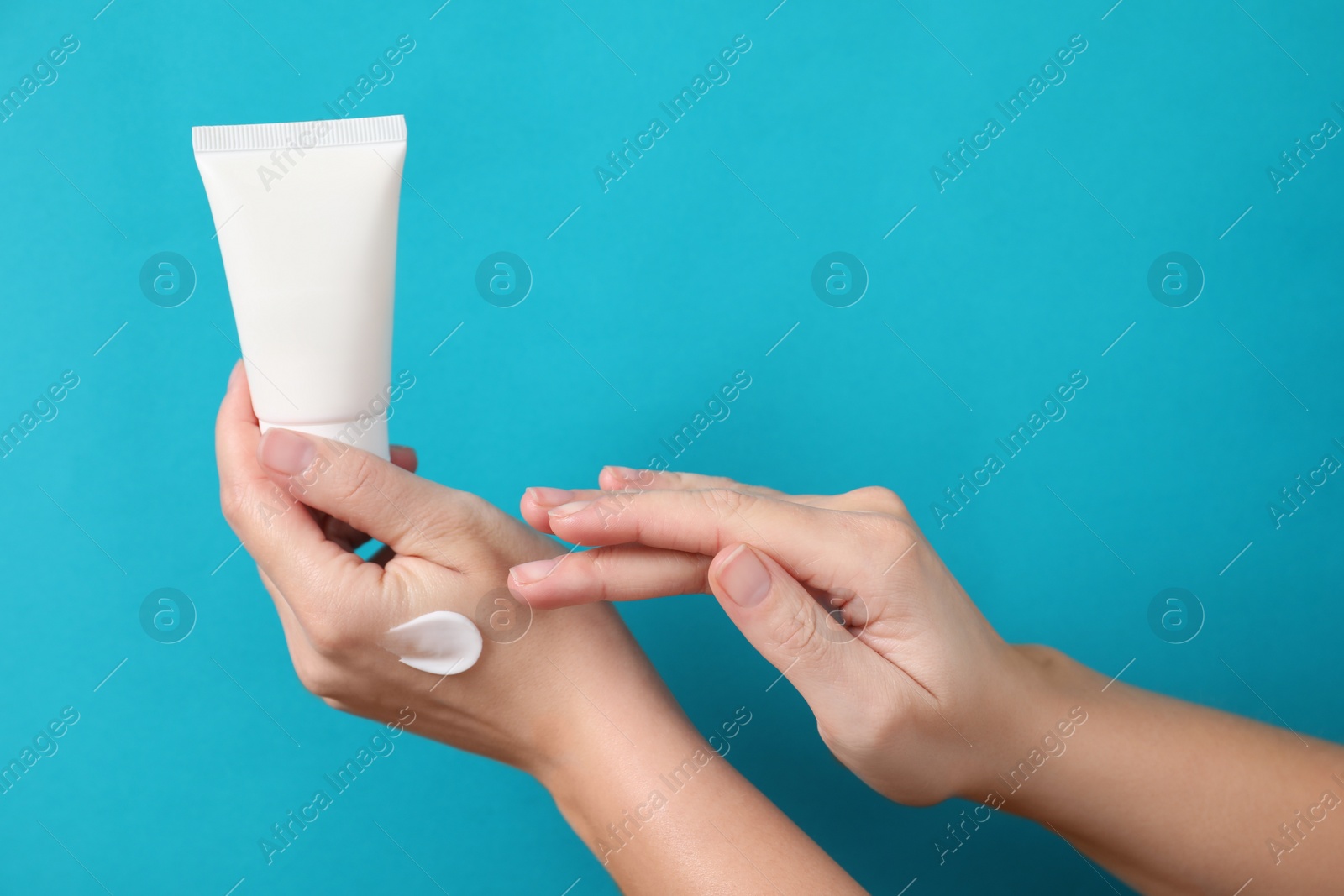 Photo of Woman with tube applying cosmetic cream onto her hand on light blue background, closeup. Space for text