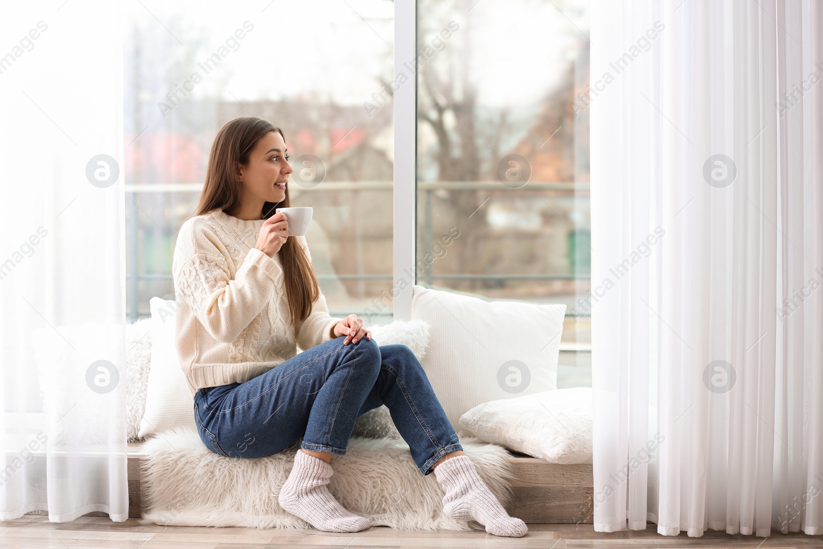 Photo of Young woman with cup near window indoors