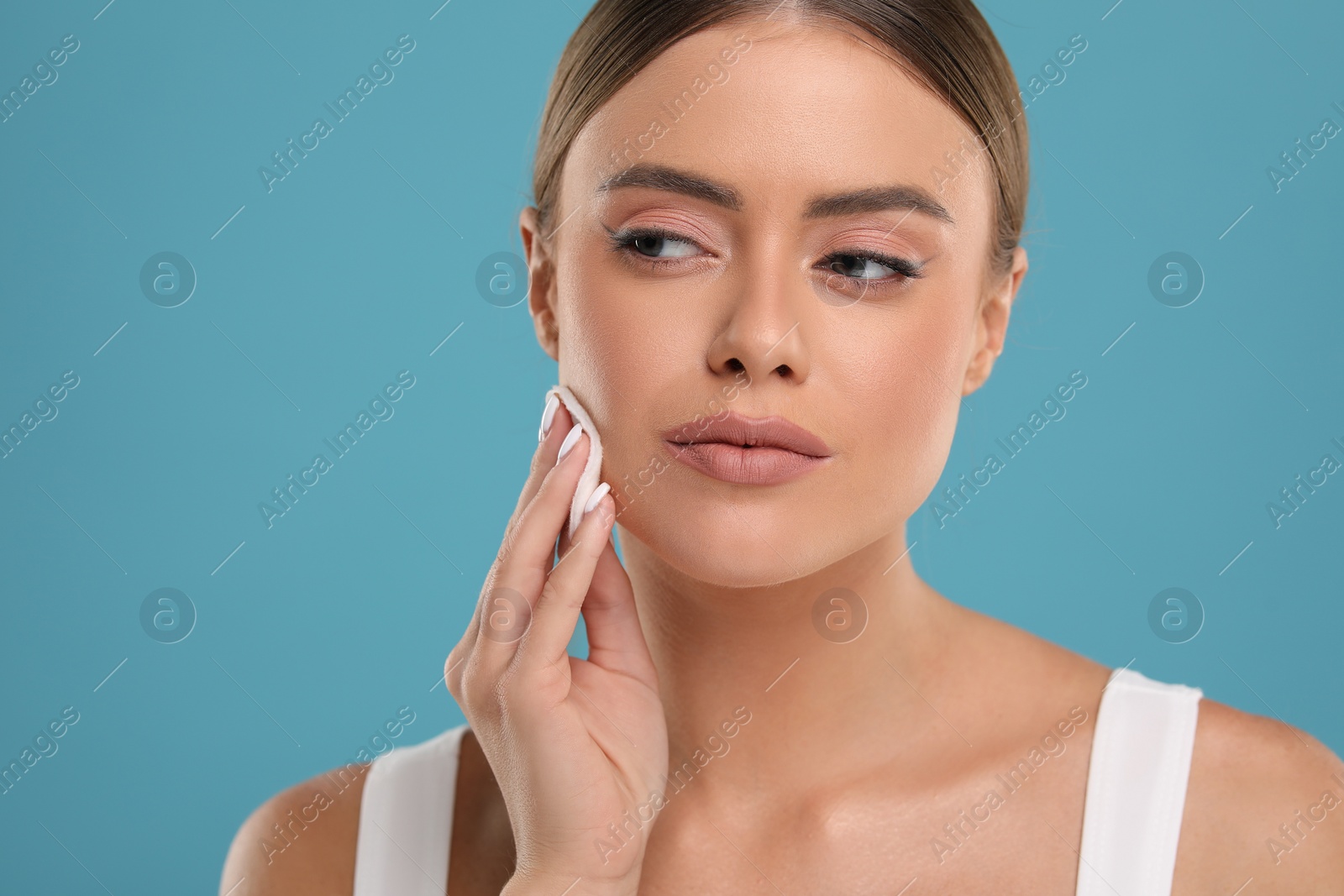 Photo of Beautiful woman removing makeup with cotton pad on light blue background, space for text