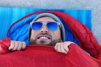 Male camper lying in sleeping bag on mat, view from above