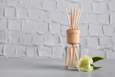 Photo of Aromatic reed freshener and flower on table against textured wall, space for text