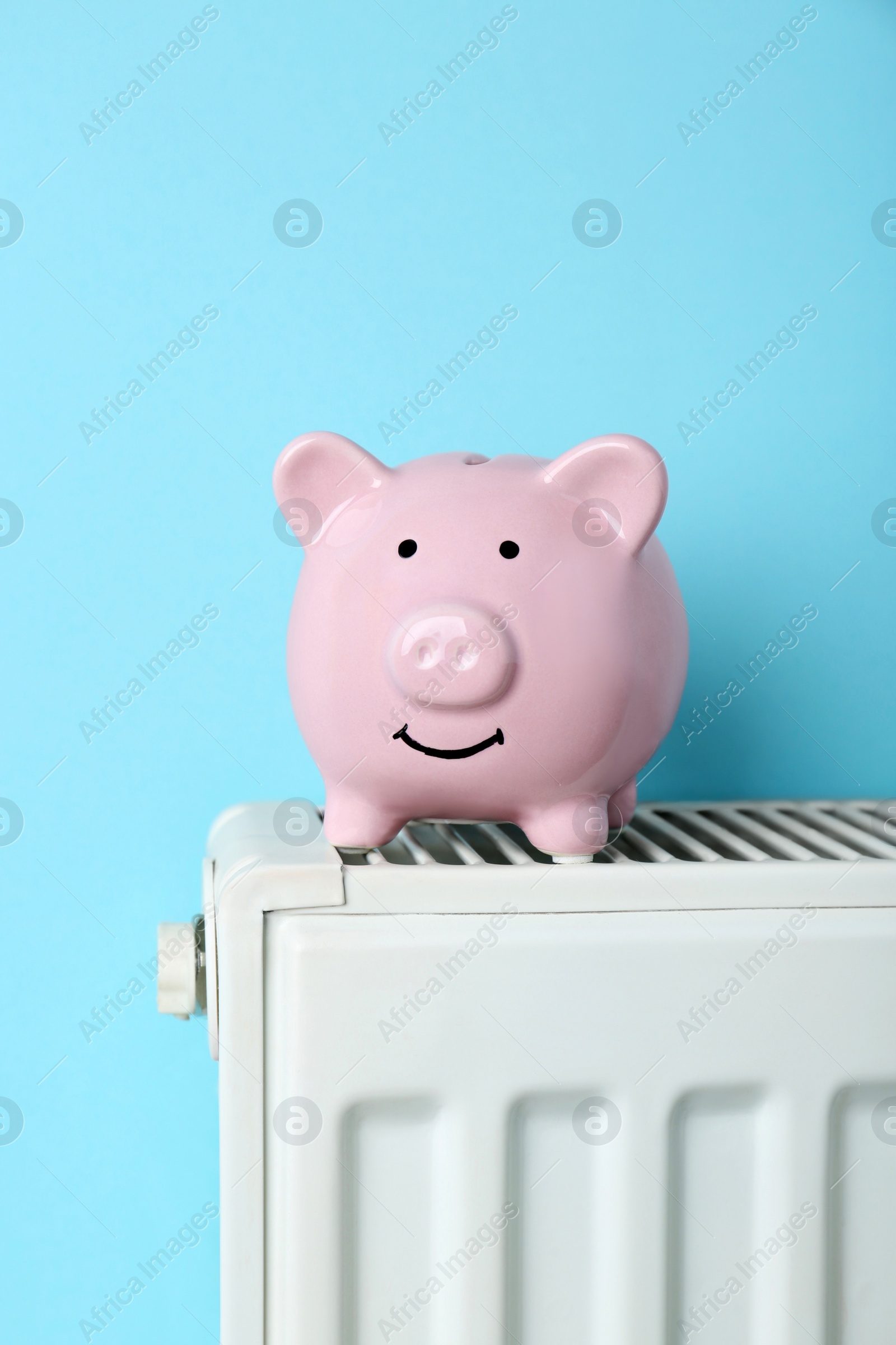 Photo of Piggy bank on heating radiator against light blue background