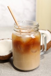 Photo of Mason jar of delicious iced coffee with coconut syrup on light grey table, closeup