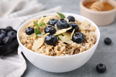 Photo of Tasty oatmeal with blueberries, mint and almond petals in bowl on grey table, closeup