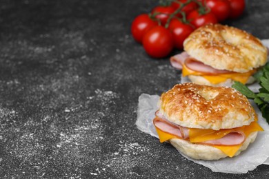 Photo of Delicious bagels with ham and cheese on dark grey textured table, space for text