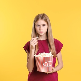 Emotional teenage girl with popcorn during cinema show on color background