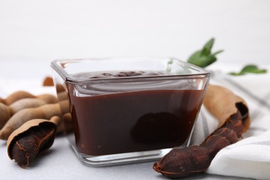 Photo of Bowl of tasty tamarind sauce and fresh pods on light table, closeup
