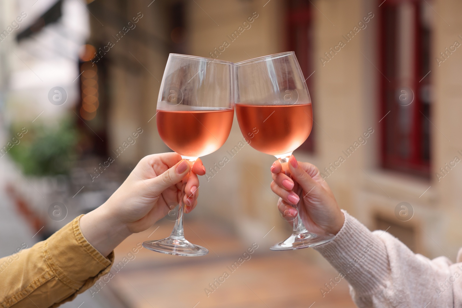 Photo of Women clinking glasses with rose wine outdoors, closeup