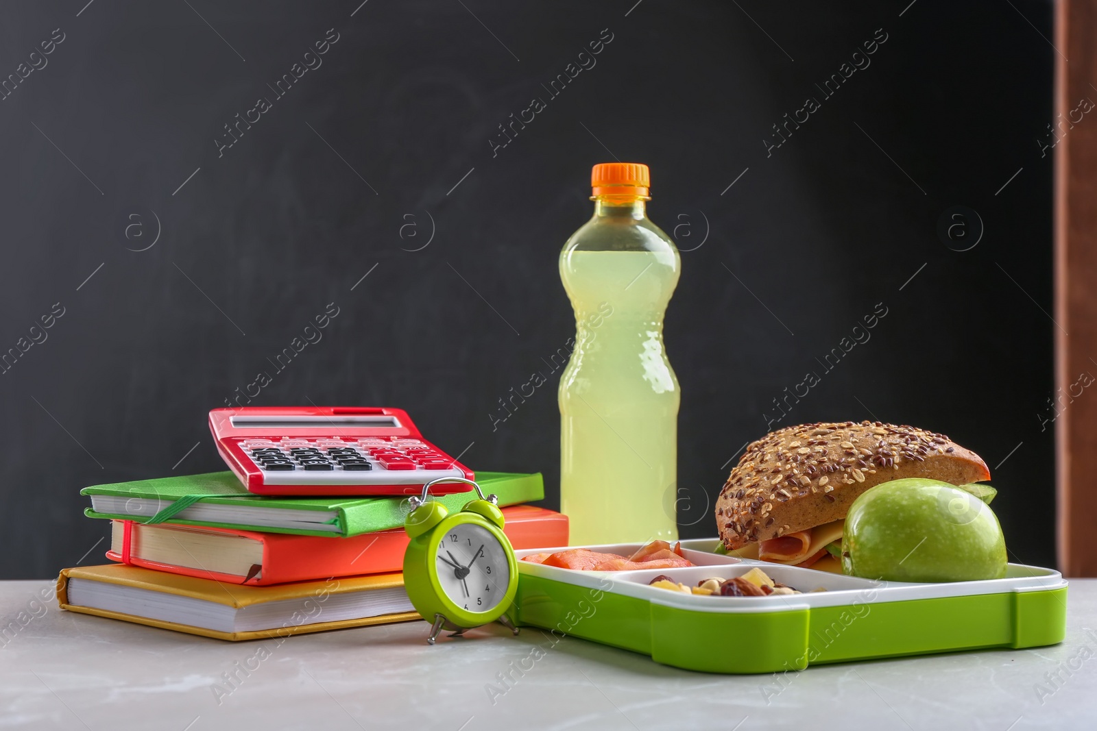 Photo of Composition with lunch box and food on table against blackboard