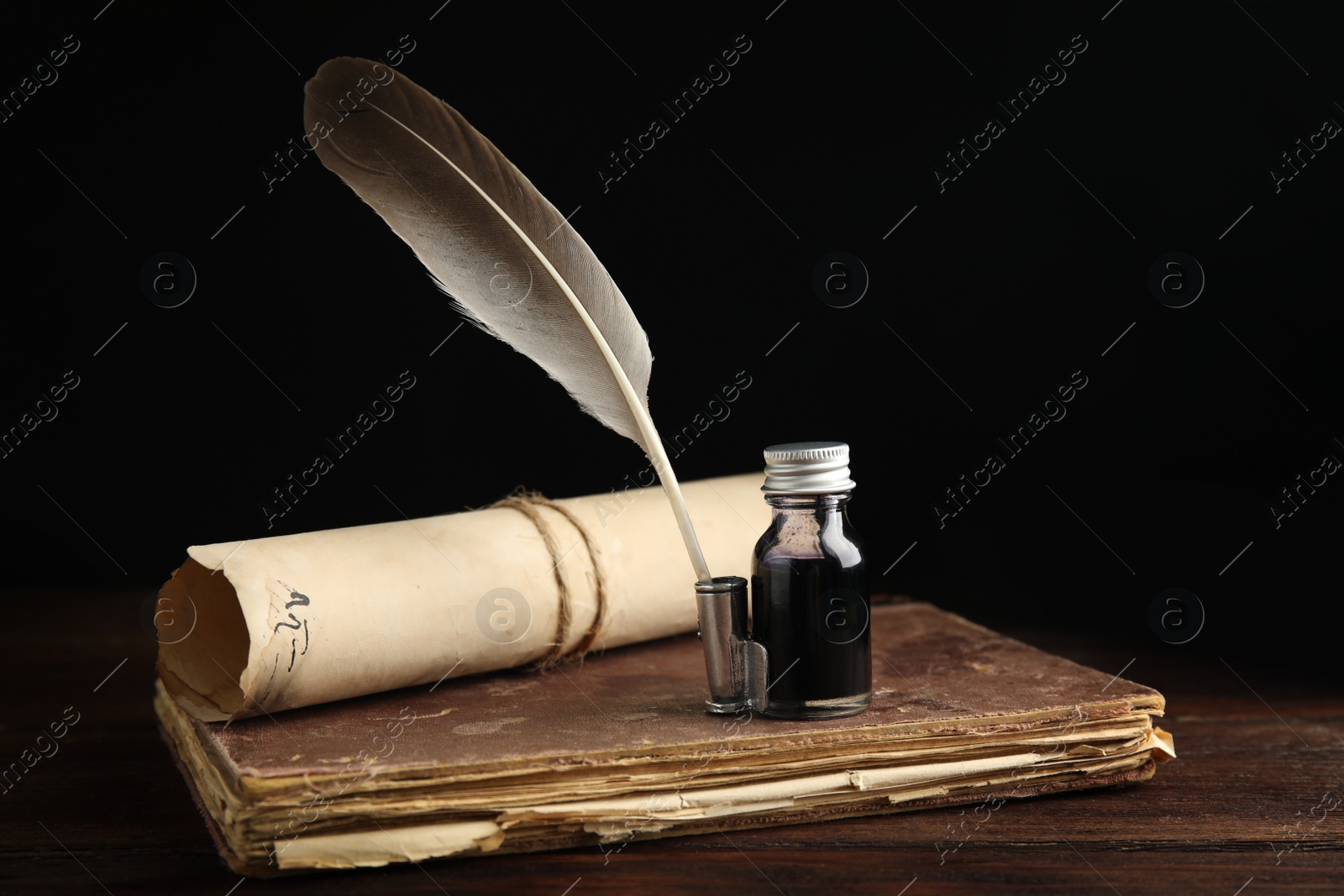 Photo of Feather pen, bottle of ink, old book and parchment scroll on wooden table